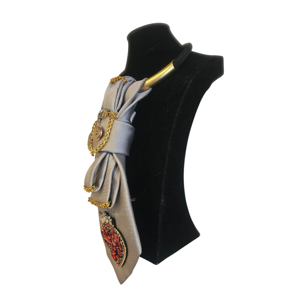 Cravatta gioiello donna componibile grigio chiaro con cuore ex voto rosso, strass e catene metalliche su manichino nero verso destra